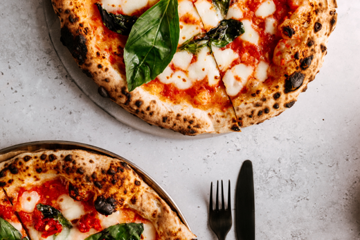 Two beautiful margherita pizzas pictured from above on marble table with knife and fork at Bishopton Restaurant il posto
